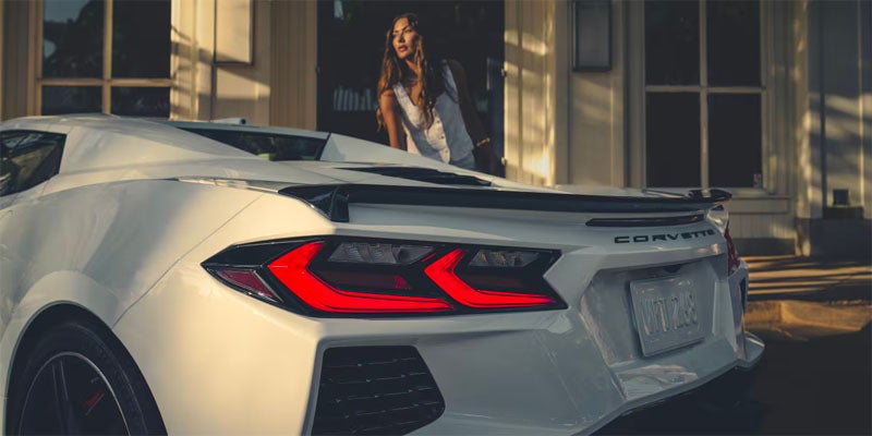A woman stands beside a sleek white sports car.